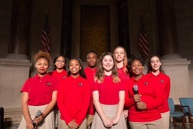 Außenansicht des Radio City Music Hall in New York City bei Nacht, hell erleuchtet und umgeben von hohen Gebäuden, mit einem 'Radio City'-Schild und zusätzlichen Schildern auf der rechten Seite.