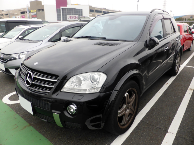Schwarzer Mercedes-Benz ML 350 CDI Blueefficiency geparkt auf einem Parkplatz mit Gebäuden, Masten, Bäumen und einem klaren blauen Himmel.