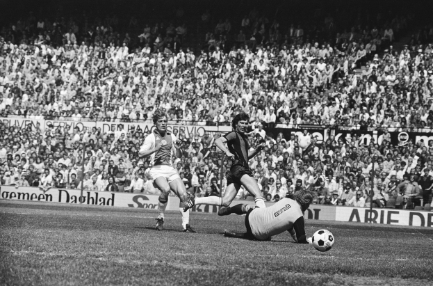 Schwarzes Foto von Männern, die auf einem Feld Fußball spielen, mit Zuschauern im Hintergrund und einem Banner der Bundesliga 1978-79.