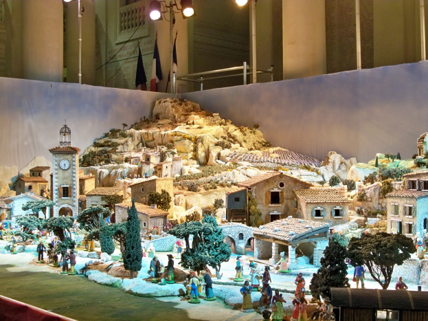 Ein detailliertes Miniatur-Modell einer Krippe, das in einem Museum ausgestellt wird und Figuren, Strukturen und Beleuchtung enthält.