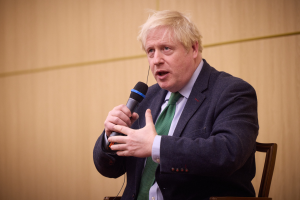 Ein Mann im Anzug und Krawatte sitzt in einem Stuhl und hält ein Mikrofon, während er in eine Diskussion vertieft zu sein scheint.