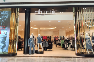 Ein stylischer Modeboutique in einem Einkaufszentrum mit Schaufensterpuppen in der neuesten Mode, Kleidung an Bügeln, einer Säule, einem Schild, Deckenlampen und einem Fliesenboden.