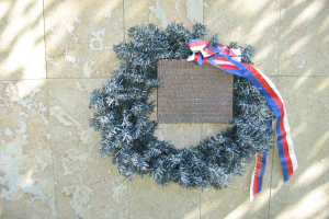 Ein Kranz mit einer rot-weiß-blauen Schleife an einer Gebäudewand, mit einer Inschrift versehen.
