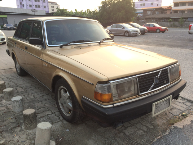 Ein goldfarbener Wagen, der an der Straßense geparkt ist, umgeben von Gebäuden, Bäumen und einem klaren blauen Himmel.