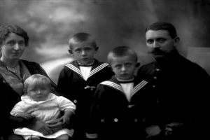 Ein Schwarz-Weiß-Foto einer Familie, die posiert, mit einer Frau, die ein Baby im Arm hält und zwei Jungen neben ihr, vor einem unscharfen Hintergrund.