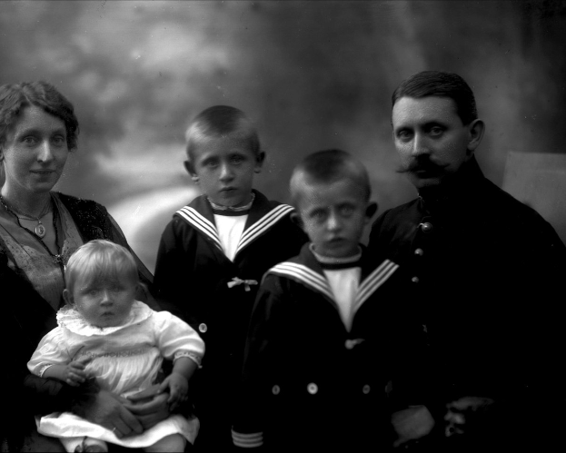 Ein Schwarz-Weiß-Foto einer Familie, die posiert, mit einer Frau, die ein Baby im Arm hält und zwei Jungen neben ihr, vor einem unscharfen Hintergrund.