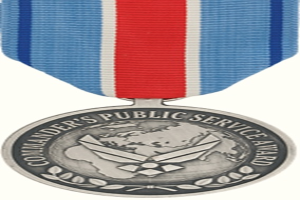 Eine Silbermedaille mit einer rot-weiß-blauen Schleife, auf der der Text 'Kommandeur's Public Service Award' auf einem weißen Hintergrund zu sehen ist.