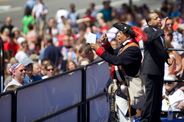 Ein Mann in Piratenkostüm steht auf einer Bühne und hält ein Blatt Papier in der Hand, vor ihm eine Menschenmenge und im Hintergrund unscharfe Geländer.