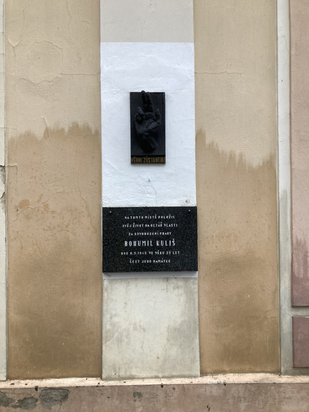 Schwarze Tafel an einem Gebäude mit einer darauf ruhenden Hand, die wahrscheinlich Holocaust-Opfern gedenkt.