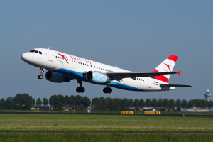 Airbus A320-200 der Austrian Airlines startet vom Frankfurter Airport mit grünem Gras darunter, Bäumen und Gebäuden im Hintergrund und einem Turm auf der rechten Seite.