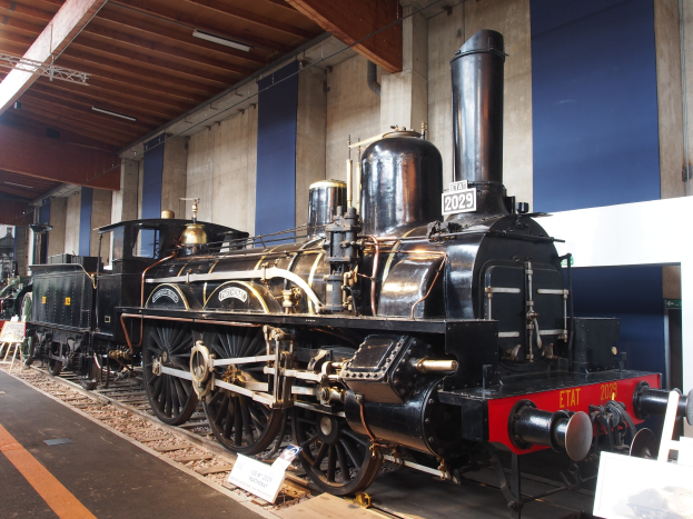 Alte Dampflokomotive in einem Museums Setting mit umliegenden Eisenbahnschienen, Informationsschildern und Beleuchtungsk├Ârpern.
