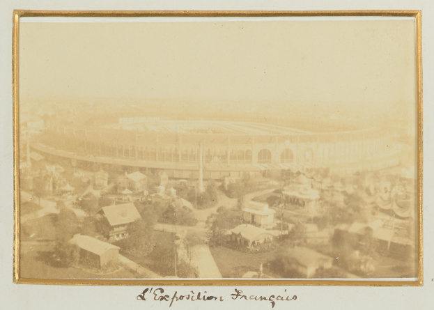 Altes Schwarz-Weiß-Foto eines Stadions inmitten einer Stadt, umgeben von Gebäuden, Bäumen und Strommasten, mit Text am unteren Rand.