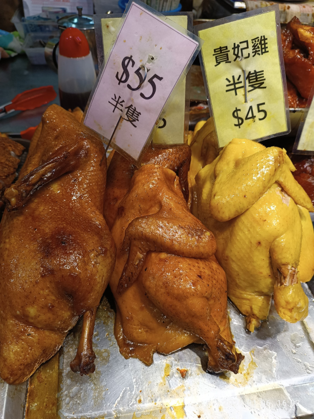 Eine Gruppe von Hühnern auf einem Metalltablett mit Preisschildern in einem belebten Markt.